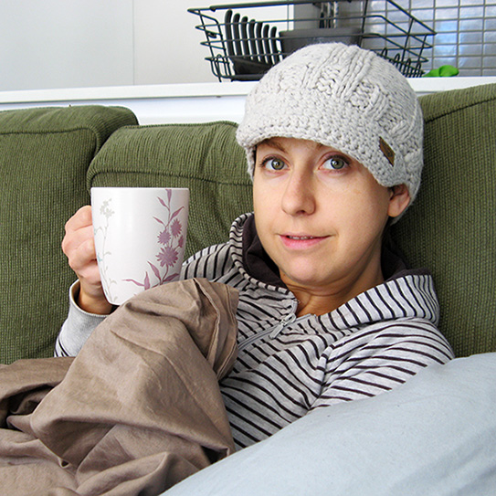 woman wearing beanie on couch and holding coffee mug