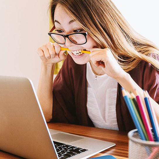 woman looking at computer and chewing on pencil