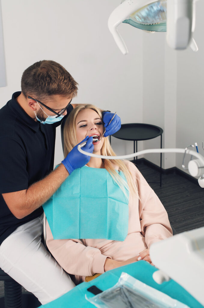 Portrait of a dentist in eyeglasses who treats teeth of young blond woman patient.