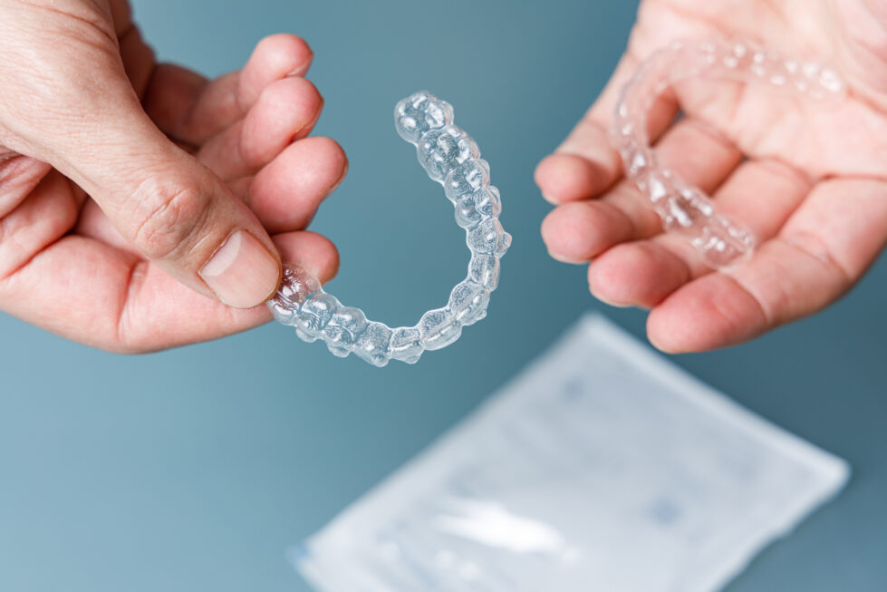 Hands holding a set of clear Invisalign dental aligners