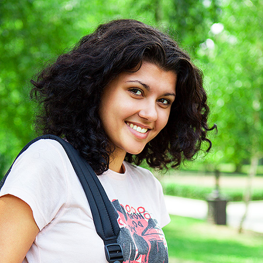 woman with backpack on her shoulder, smiling at camera