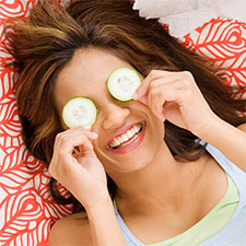 woman smiling with cucumbers on her eyes